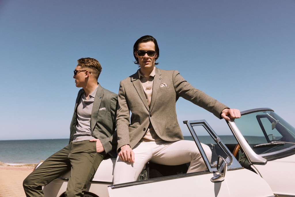 Two men in suits on white car for summer collection.